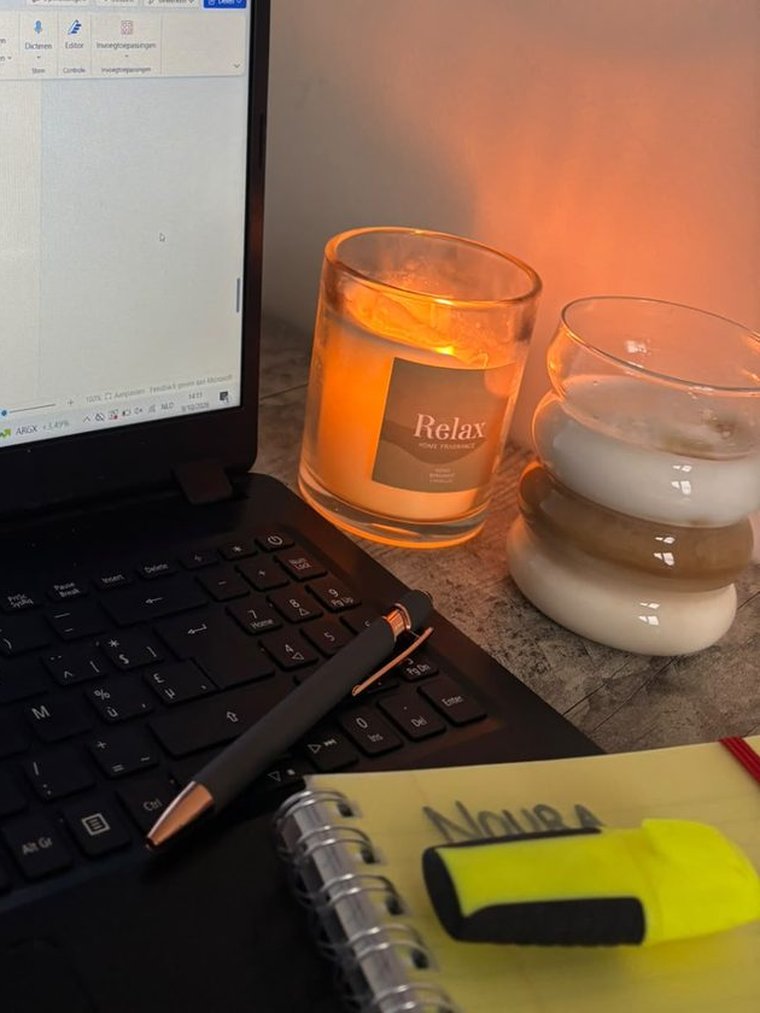 Mijn werkplek: een laptop, een brandende kaars en een schrift met mijn naam